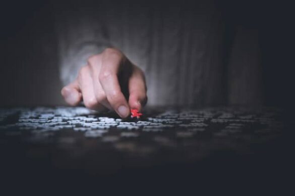 A hand holding one red puzzle piece amongst a table of white puzzle pieces